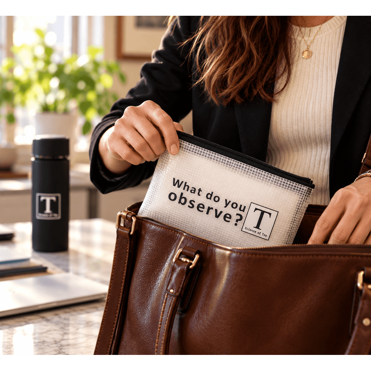 Science of Tea travel pouch being packed into a leather work bag, with a tumbler softly blurred behind