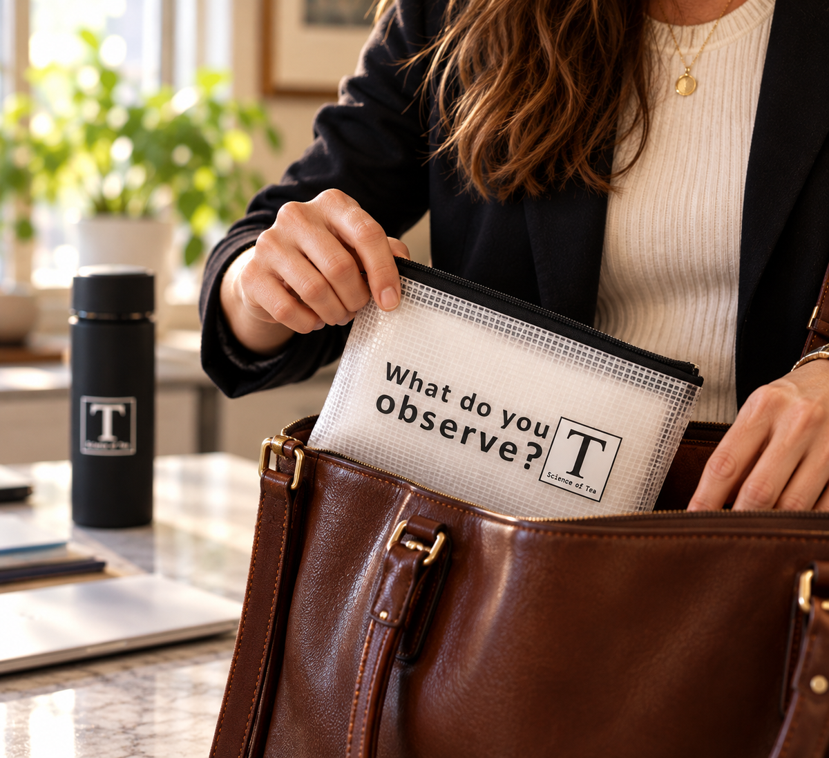 Science of Tea travel pouch being packed into a leather work bag, with a tumbler softly blurred behind
